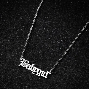 Vue macro du collier Babygirl argenté avec police gothique sur fond texturé sombre