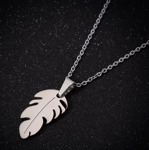 Collier minimaliste avec pendentif feuille en argent mat sur un fond noir texturé