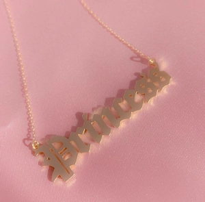 Makro-Detail der vergoldeten Princess-Buchstaben-Halskette auf pinkfarbenem Stoff