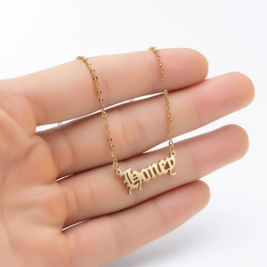 Close-up of golden stainless steel Honey pendant necklace in gothic font held by hand