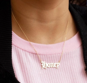 Detail shot of the golden Honey pendant necklace in vintage font worn by a model