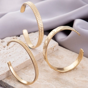 Set of three textured gold stainless steel open bangles on elegant stone surface