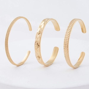 Detailed view of three gold vintage stackable cuff bracelets with star and wheat engravings