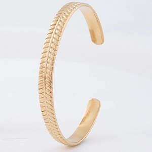 Detailed close-up of a gold-plated C-shaped cuff bracelet with intricate leaf-like textures