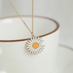 Collier marguerite minimaliste avec pétales blancs et chaîne dorée sur une tasse