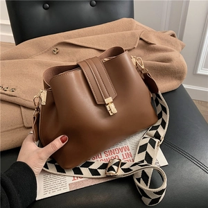 Caramel leather bucket bag with geometric wide strap and gold buckle on a stylish coat