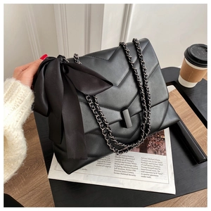 Detail view of large quilted black shoulder bag with chain strap and oversized silk bow