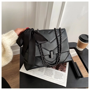 Close-up of black quilted leather shoulder bag with a large decorative silk bow detail
