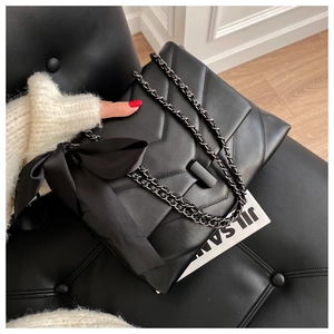 Close-up of black quilted shoulder bag featuring metal chain and large side bow detail