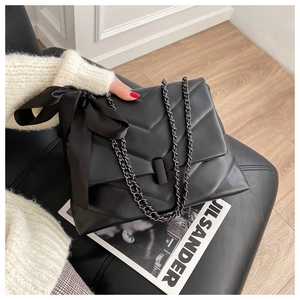 Detail of black quilted chain bag featuring a large satin bow and premium leather texture