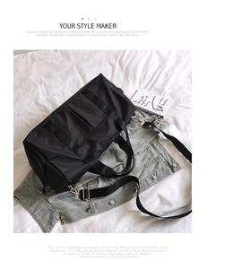 Close-up of black nylon gym bag with gold hardware and adjustable strap on a bed