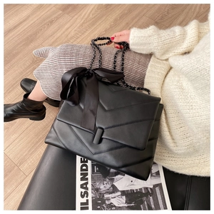 Detail of black quilted chain bag with V-shaped stitching and silk bow decoration