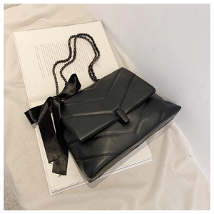 Detail of black V-quilted shoulder bag with elegant silk bow and matte chain strap