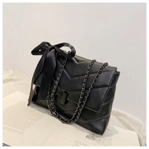 Detail of black V-quilted shoulder bag with large satin bow and sleek metal chain strap