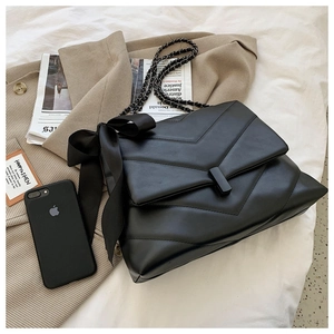Detail of black chevron quilted leather bag with elegant ribbon bow and chain strap