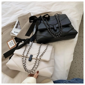 Detail of quilted chain bags with elegant bows in black and cream on fabric