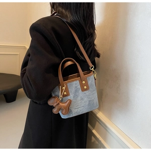 Detail of blue denim tote bag with brown leather handle and puppy charm accessory