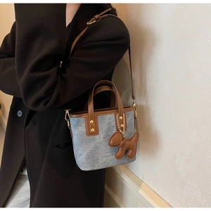 Detail of blue matte bucket bag with brown leather trim and cute puppy charm accessory