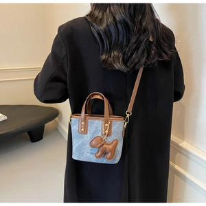 Detail of denim and leather bucket bag with cute puppy charm and adjustable strap