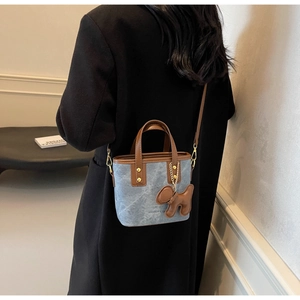 Detail of light blue denim crossbody bag with brown leather trim worn with a black coat