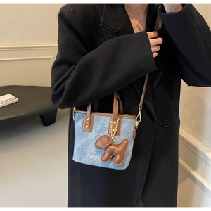 Detailed look at denim and leather mini bucket bag with a cute puppy charm accessory
