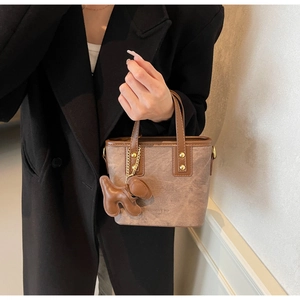 Close-up of brown textured bucket bag with puppy charm and golden rivet accents