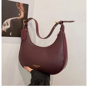 Macro view of burgundy pebble leather texture and gold logo detail on hobo bag
