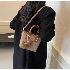 Close-up of a retro monogram crossbody bucket bag with bear charm on a female model