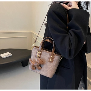 Retro brown bucket bag worn by model with leather puppy charm and metal chain detail