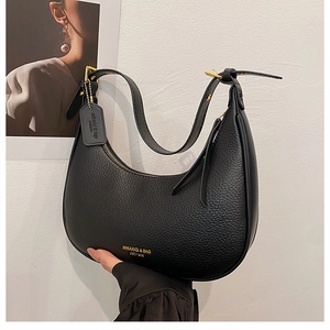Detail of black lychee grain leather crescent bag with golden brand logo and strap