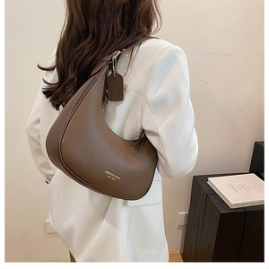Detailed view of dark brown pebbled leather shoulder bag with gold logo on a model