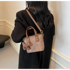 Detail of vintage brown bucket bag with gold rivets and cute dog charm on black coat