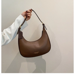Detail of brown lychee leather texture and golden metal buckle on crescent shoulder bag