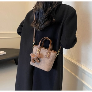 Detail of a brown suede mini bucket bag featuring a cute bear charm and top handles