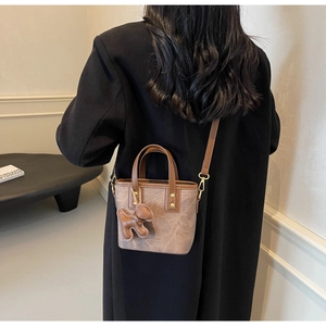 Close-up of retro brown bucket bag with plush texture, leather trim and bear charm detail