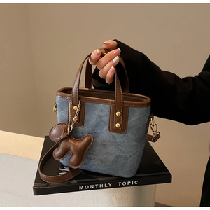 Close-up of blue denim tote bag with brown leather trim and golden rivets details