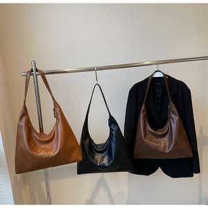 Three large soft leather tote bags in tan, black, and brown hanging on a metal display