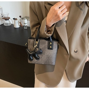 Detail of taupe bucket bag with black handle, gold hardware and cute puppy charm