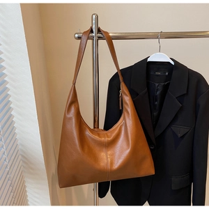 Macro shot of large caramel leather tote bag hanging on hanger against blazer background