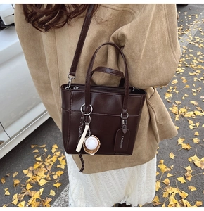 Dettaglio di una borsa tote marrone con ciondolo da baseball in una strada autunnale