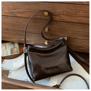 Detailansicht einer dunkelbraunen Trapez-Schultertasche mit Silberbeschlägen und Logo