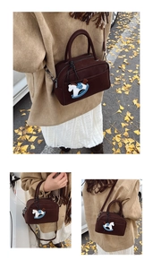 Deep brown suede handbag with horse charm shown in a cozy outdoor street setting