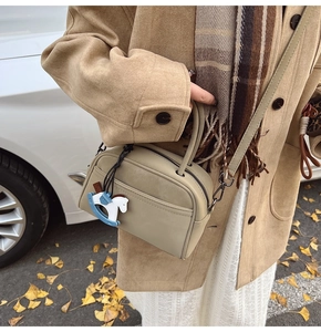 Detailed outdoor view of a khaki vintage square bag with horse charm on a coat