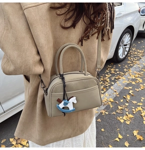 Detail of trendy small boston bag in beige leather with cute rocking horse pendant accessory