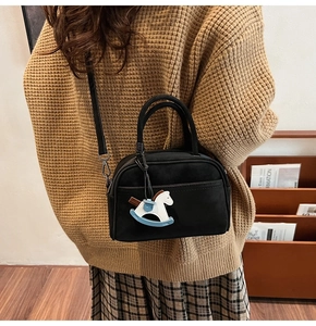 Detail of a black textured crossbody bag featuring a white horse charm on a knit sweater