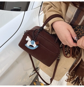 Brown Boston shoulder bag with rocking horse charm and dual zippers held by a model