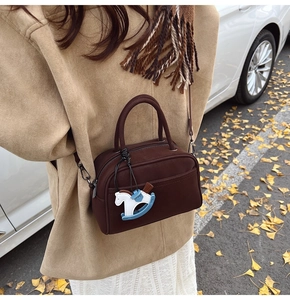 Detail of a dark brown mini bowling bag with a rocking horse charm on an autumn street