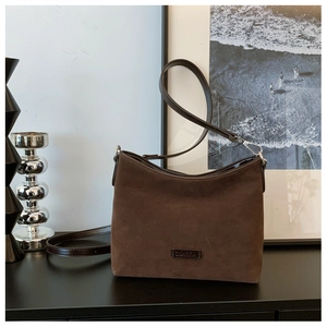 Detail der kaffeebraunen Wildledertasche mit Marken-Metallschild und Leder-Schultergurt