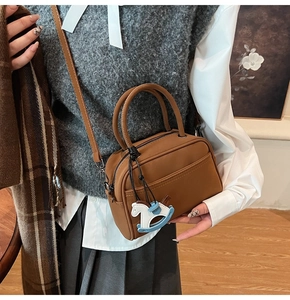 Detail of brown matte leather bowling bag with blue rocking horse charm and strap