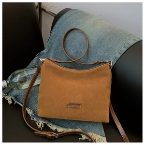 Detailaufnahme der braunen Wildleder-Schultertasche mit silbernen Beschlägen auf Denim